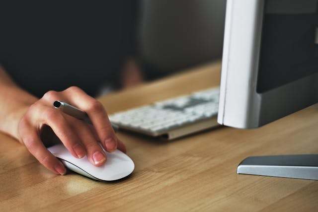 Person holding a pen while using a computer mouse